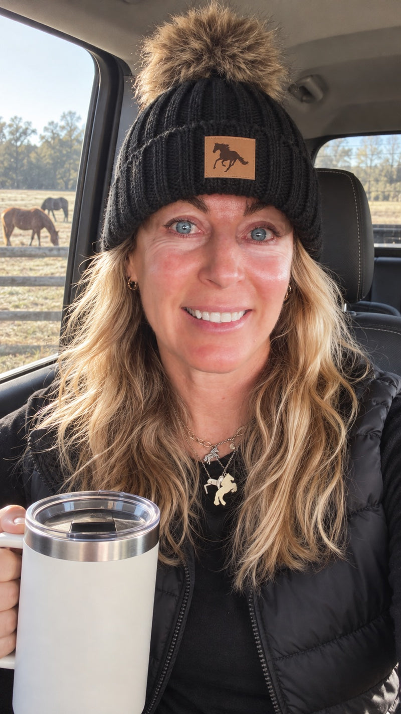 Tahlia selfie in the beanie in her truck with coffee, horses grazing outside